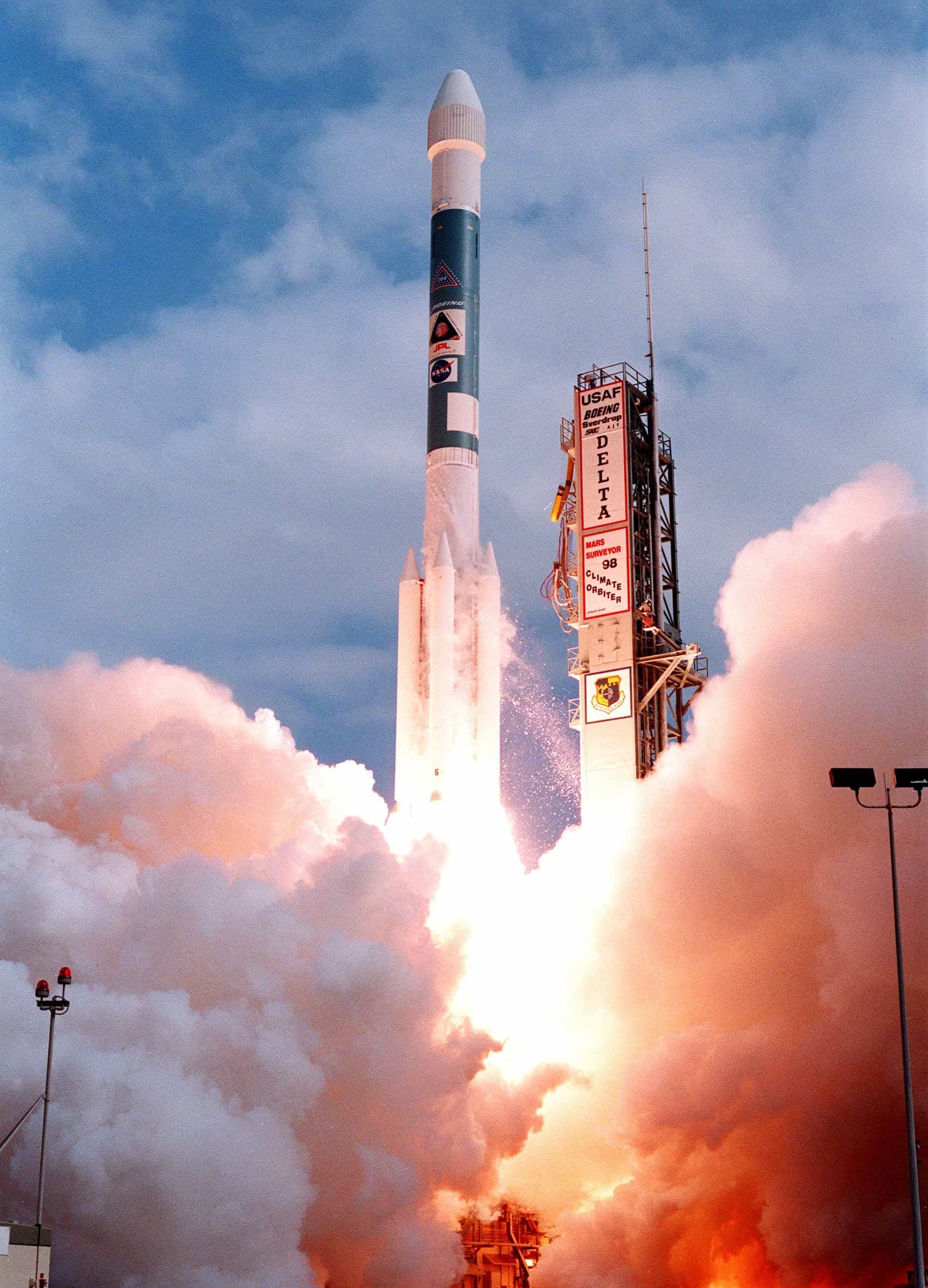 A Boeing Delta II rocket lifts off from Launch Complex 17A at Cape Canaveral on 11 December 1998, carrying NASA's Mars Climate Orbiter, amid billowing orange-lit exhaust clouds.