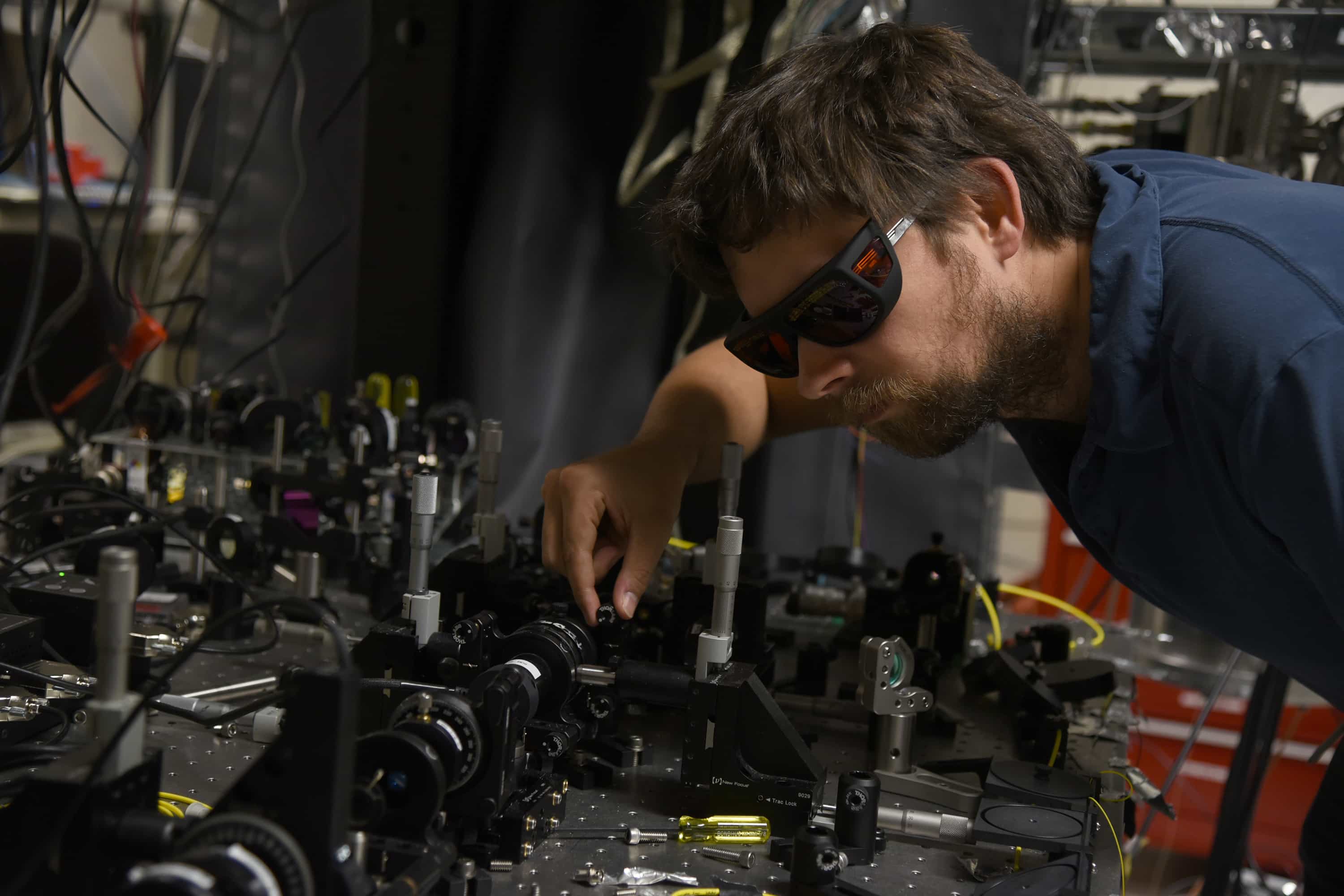 Krister Shalm, wearing tinted laser-safety glasses, leans over the optical table holding the entangled-photon source used in NIST's 2015 Bell test.