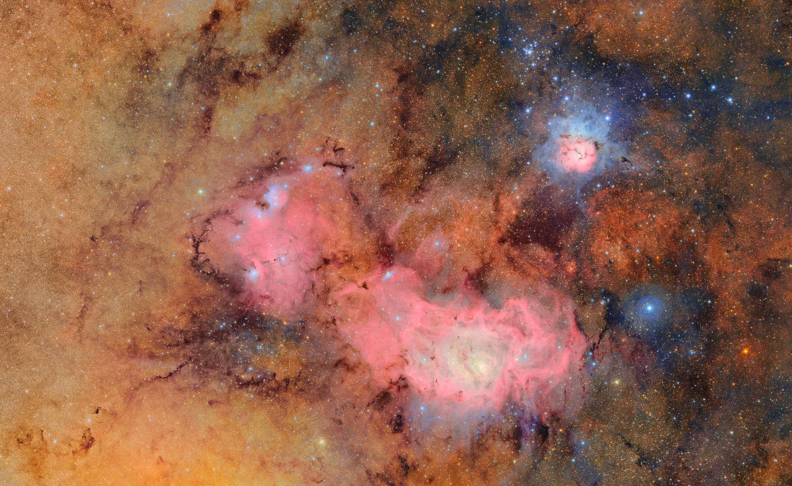 Rubin Observatory image of the Trifid and Lagoon nebulae: pink and blue glowing clouds set in a dense field of stars and dark, rust-coloured dust lanes.