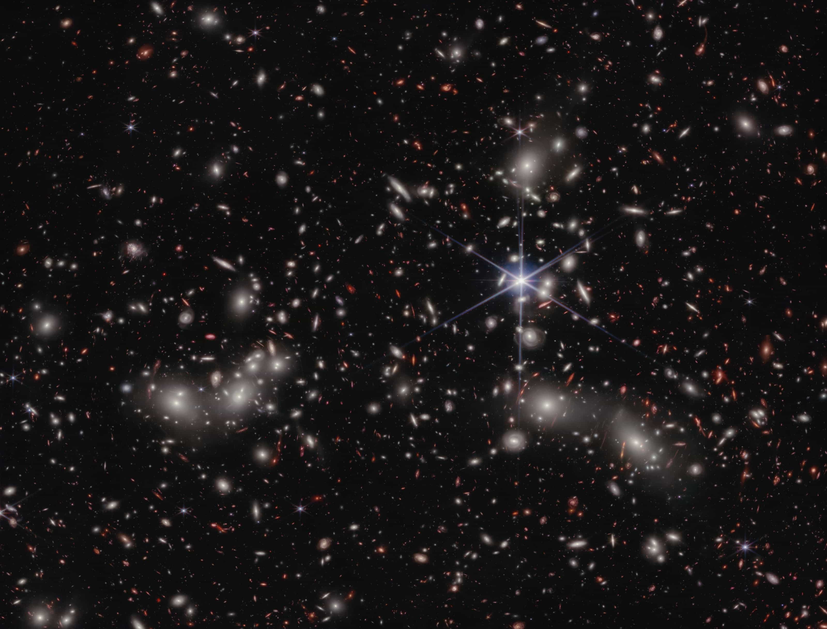 Webb image of the galaxy cluster Abell 2744: thousands of galaxies on a black background, with the cluster's bright members whose gravity bends light from more distant galaxies.